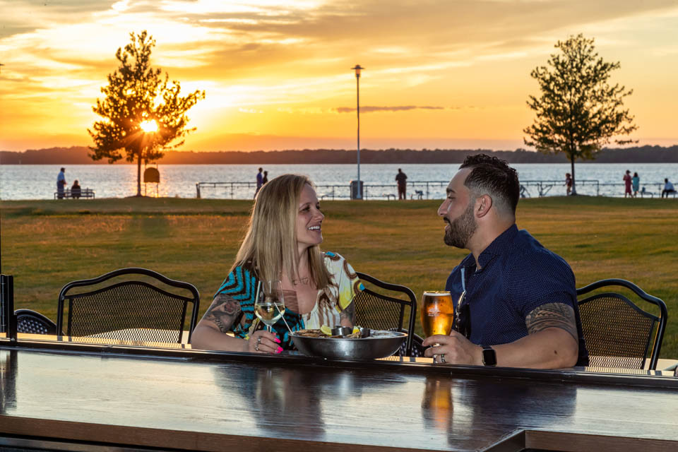 A couple enjoying evening sun near lake front holding drink glasses