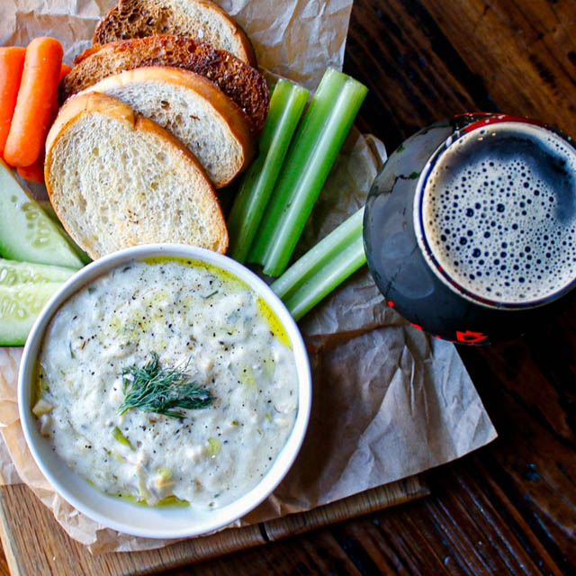 a glass filled with beer and bread, celery, cukes and dip on side